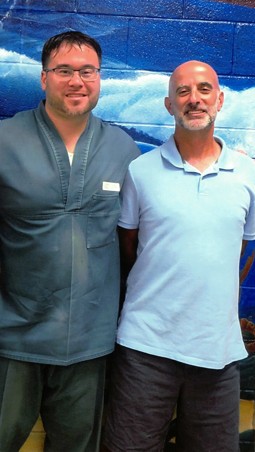 Jesse Malkin, right, standing beside Daniel Holtzclaw, left, who is wearing a prison uniform, in front of a painted wall mural.